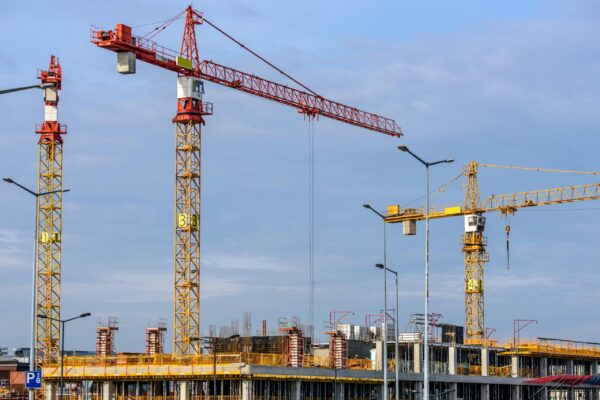 Índice Nacional da Construção Civil varia 0,88% em junho Multiple tower cranes working on a large construction site with blue sky backdrop.